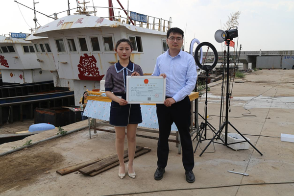 海鮮電商張夢(mèng)琴與幫辦員手持食品經(jīng)營(yíng)許可證合影。贛榆區(qū)委宣傳部供圖